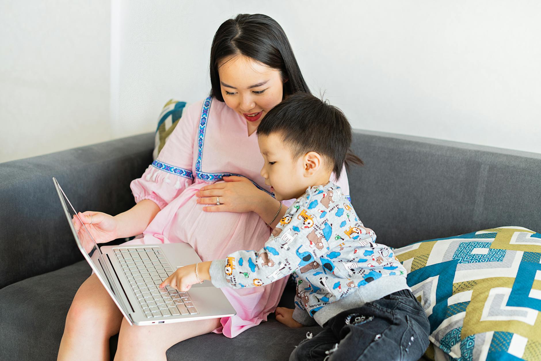 Ciężarna mama z przedszkolakiem oglądają coś na laptopie na kanapie