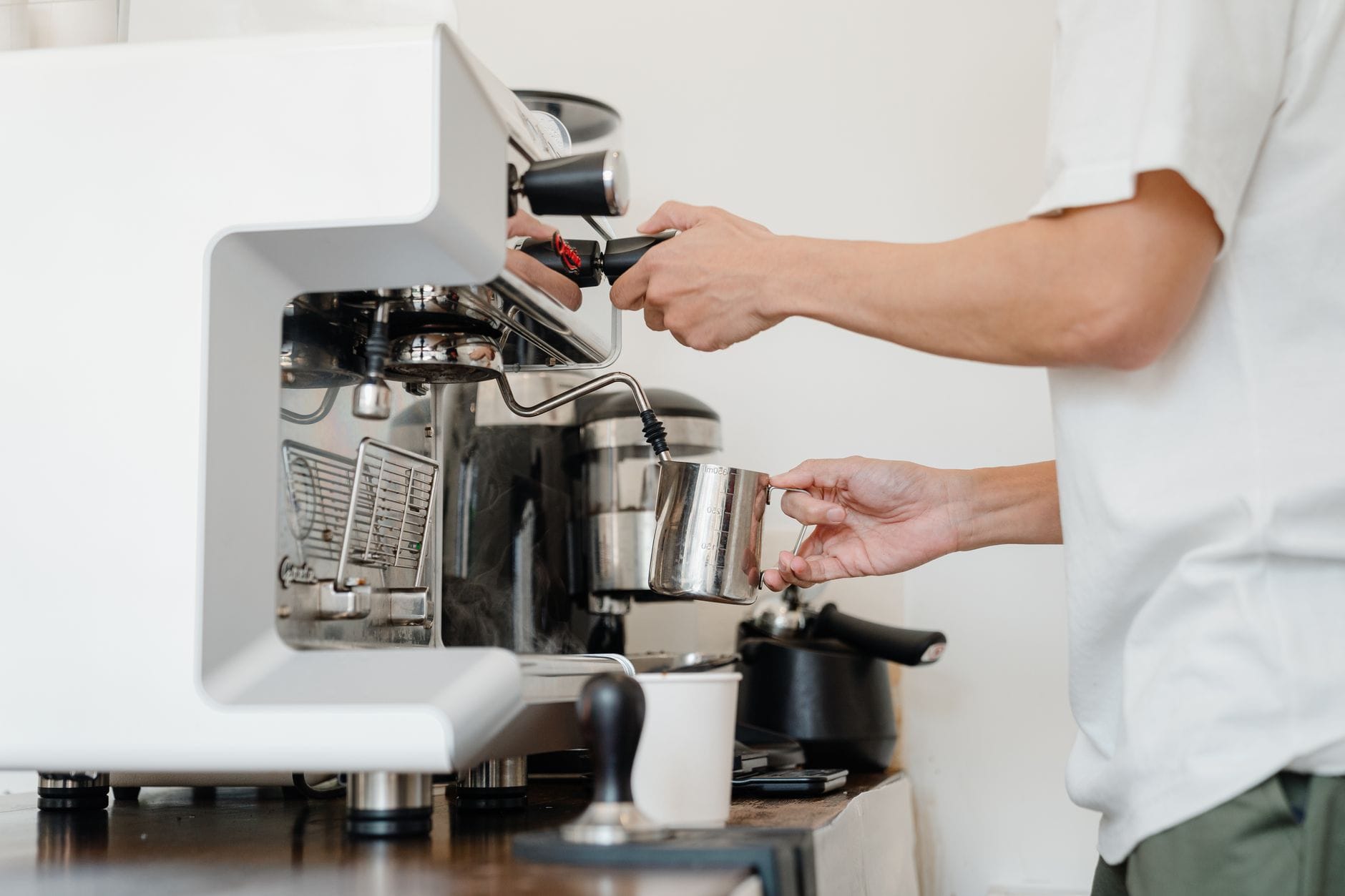 Barista spienia mleko dyszą pary ekspresu w kawiarni