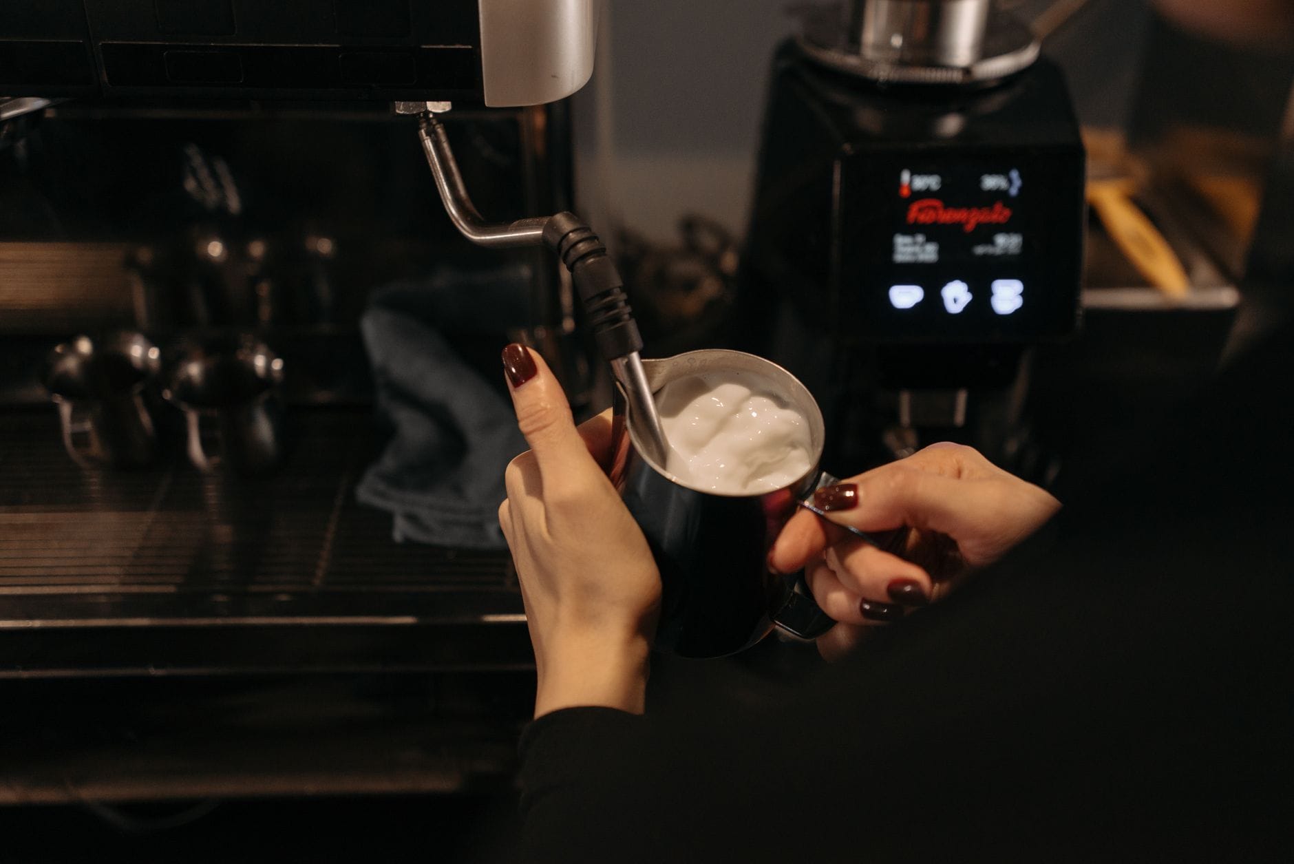 Barista spienia mleko dyszą pary w kawiarni