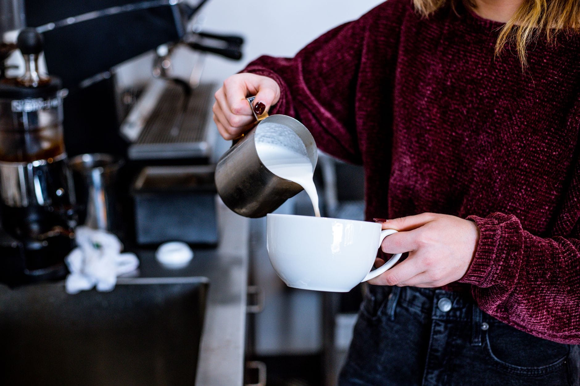 Barista w kawiarni wlewa spienione mleko do filiżanki latte Barista w kawiarni wlewa spienione mleko do filiżanki latte