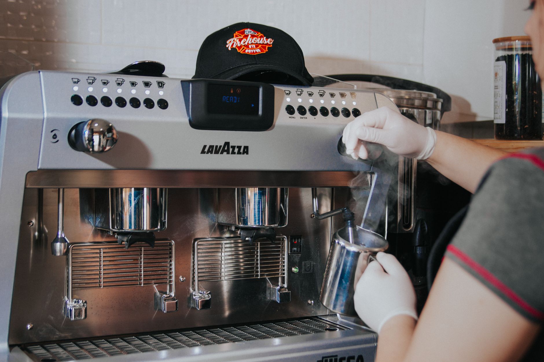 Barista w rękawiczkach spienia mleko dyszą ekspresu Lavazza